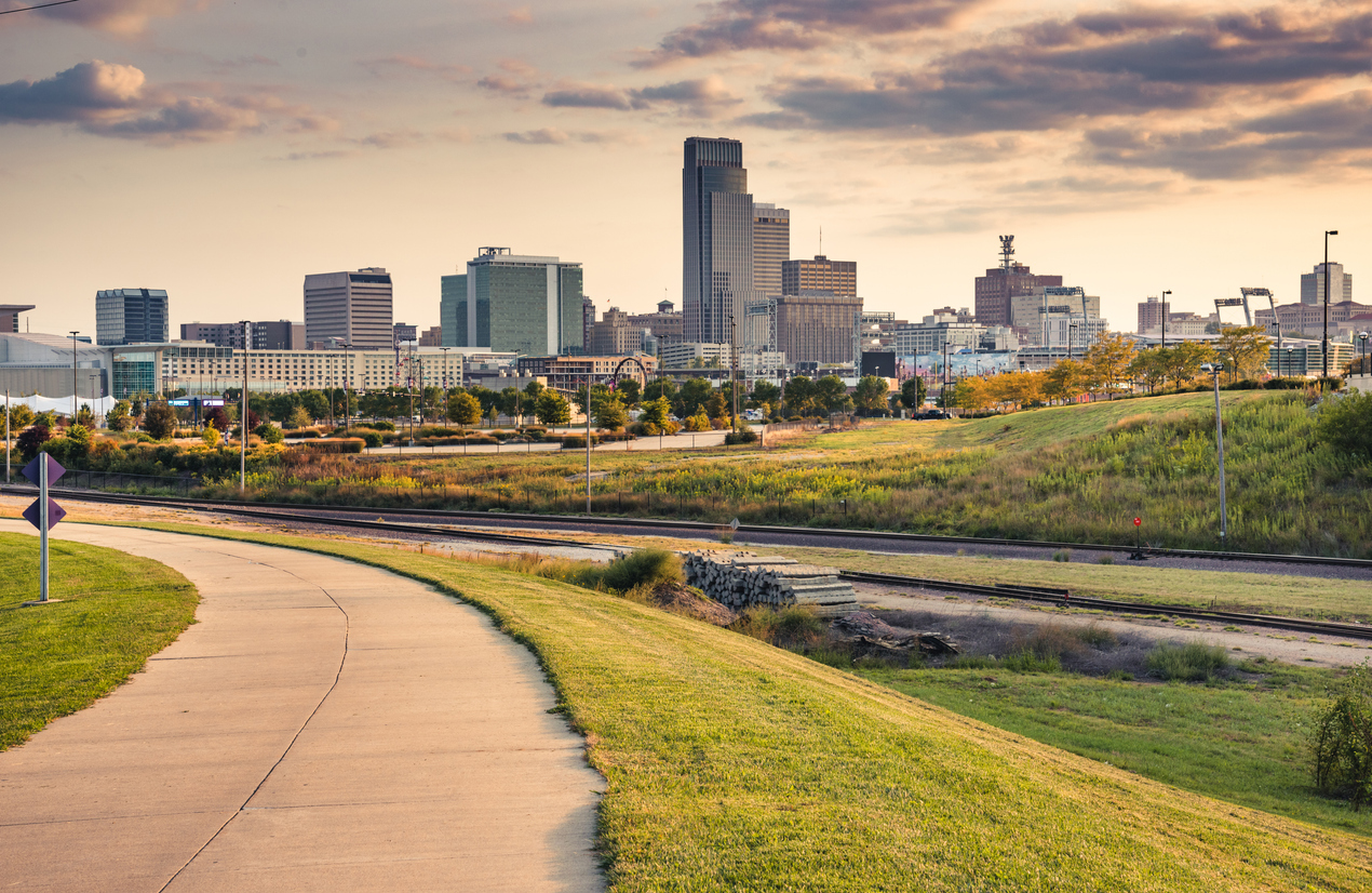 A paved path leads toward Omaha's downtown skyline at sunset.